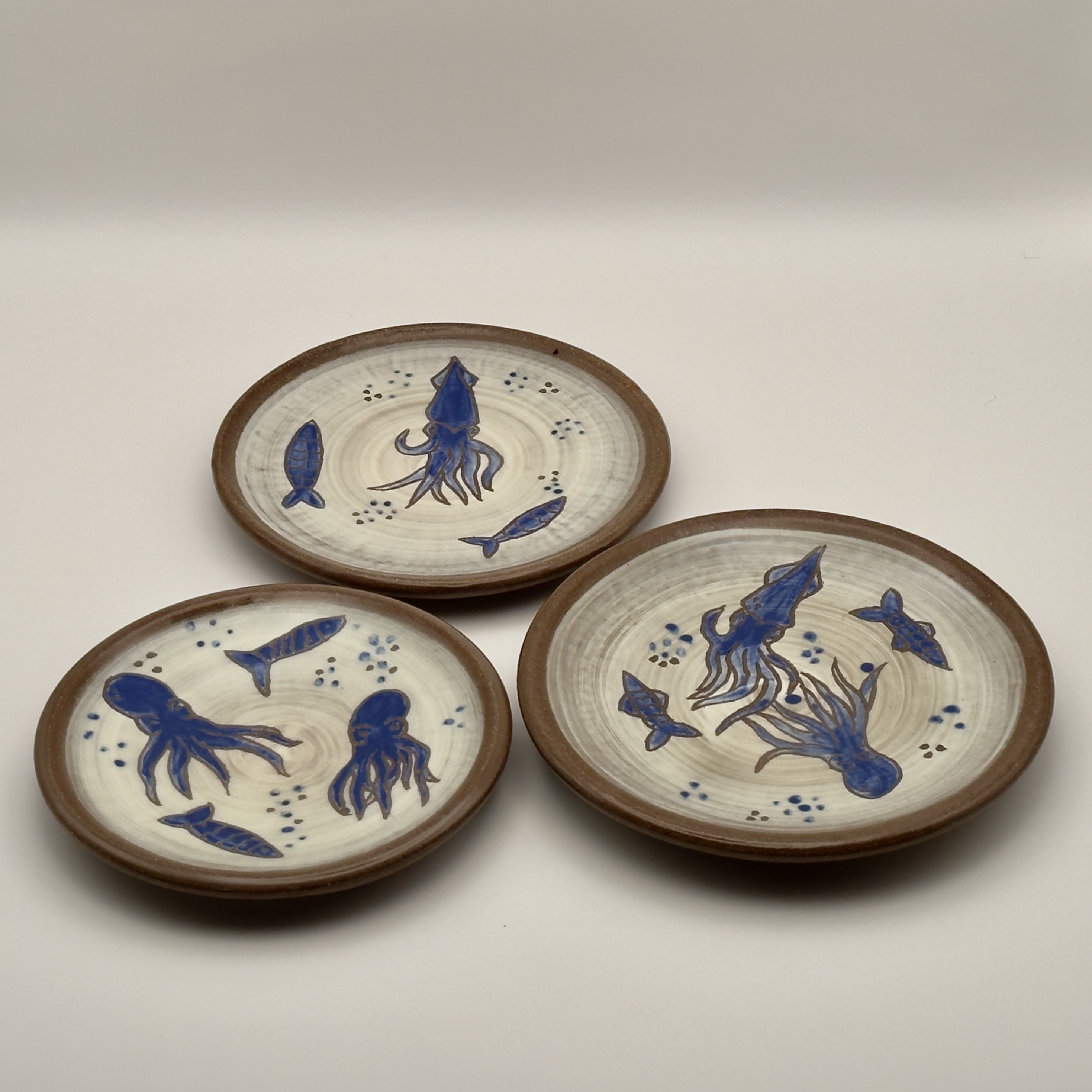 Three cream plates with hand-painted blue fish and squid designs