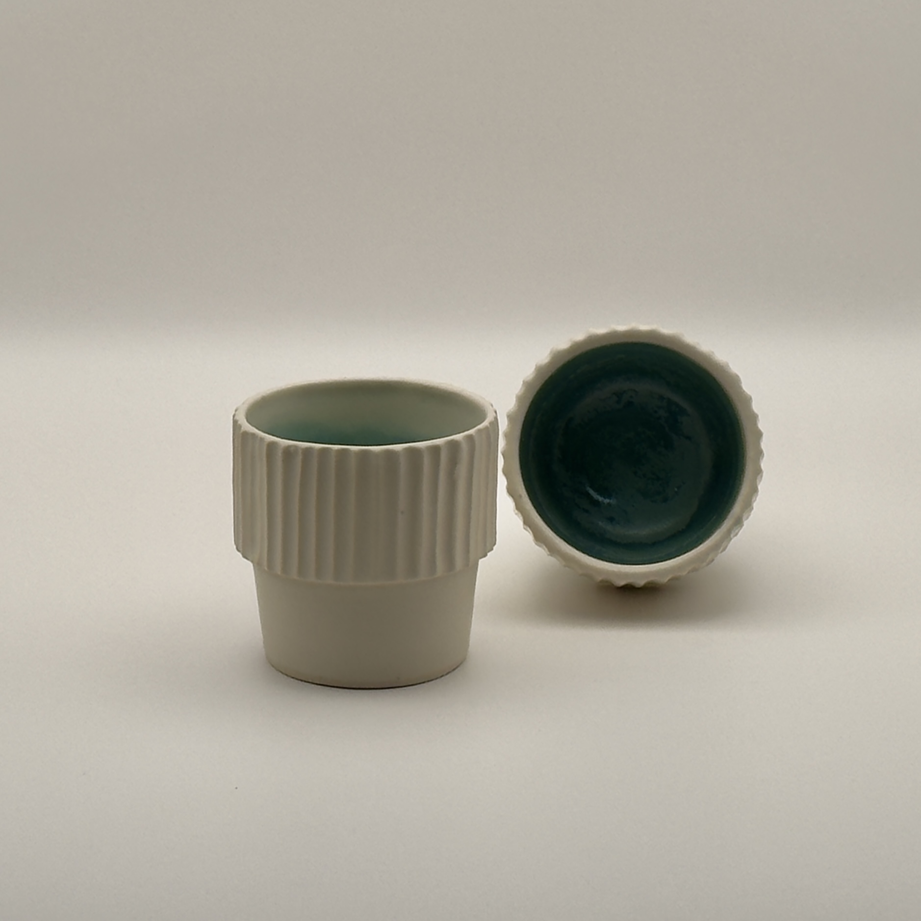 Fluted cream cup beside a tipped teal-glazed bowl