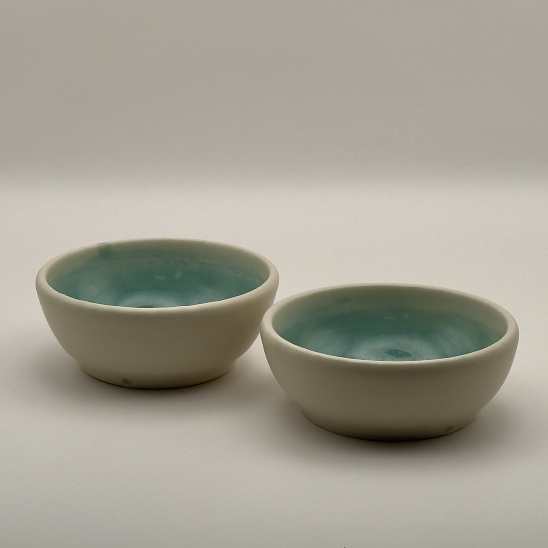Two cream bowls with teal glazed interiors, side by side