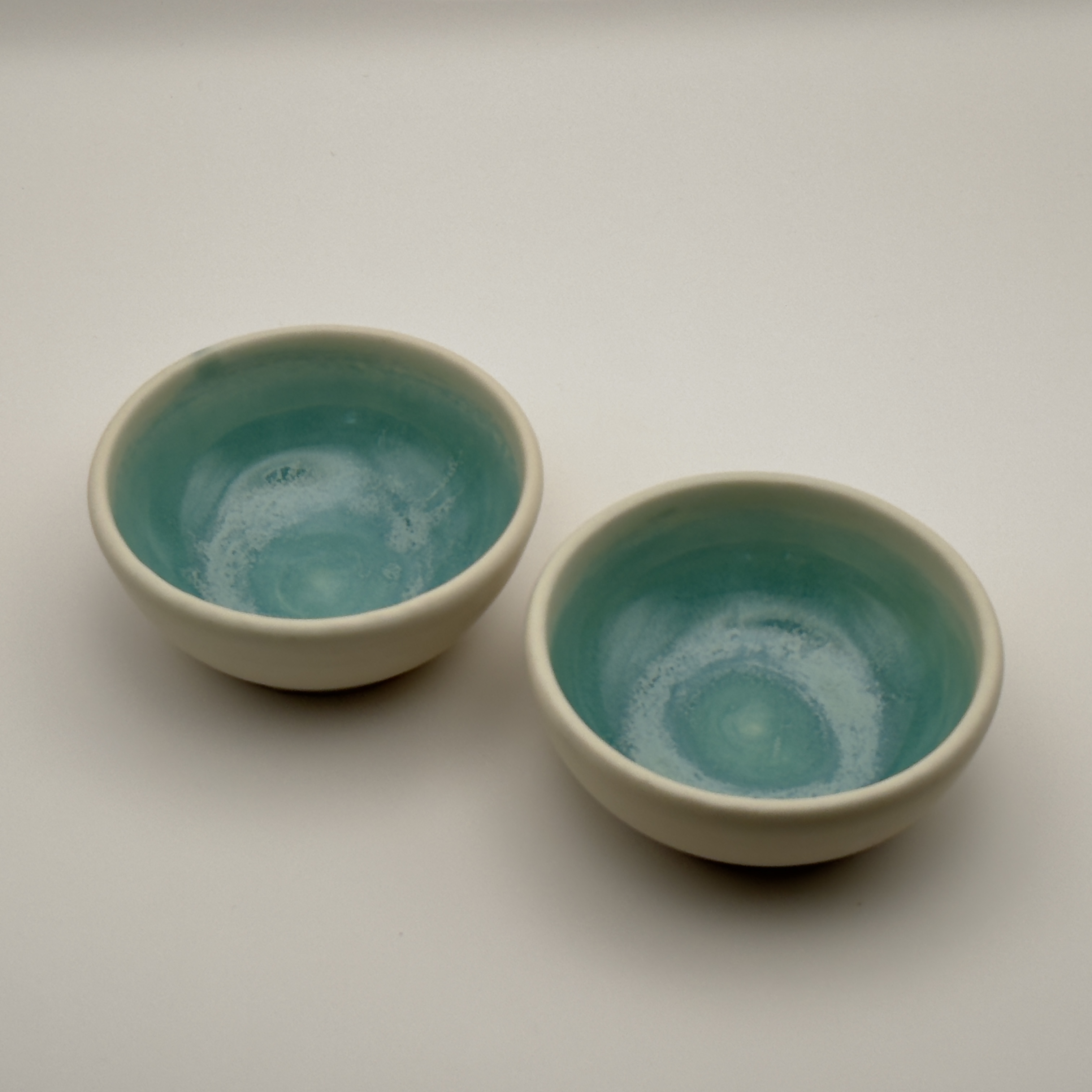 Two cream bowls with teal glazed interiors, close view